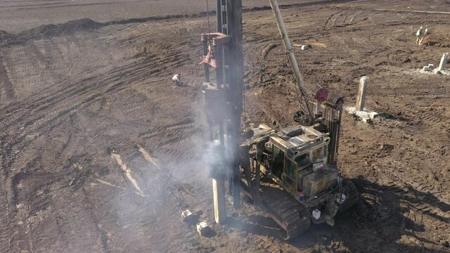 Excavation at a construction site, diesel pile driving machine with rumble and smoke drives piles deep into the ground to ensure the strength of the foundation of the future structure