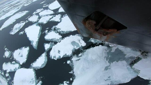 Bow of icebreaker splits ice. Water and chunks of ice. Bow and anchor. Black bow of the ship. Rusty anchor on Board. The ship goes through blue ice