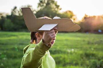 A boy in a green jacket runs across the field at sunset. The child launches a paper airplane. Happy childhood. Walking on the street without a phone.