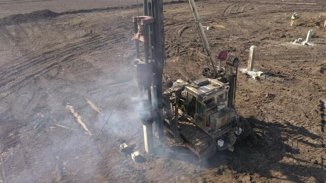 Excavation at a construction site, diesel pile driving machine with rumble and smoke drives piles deep into the ground to ensure the strength of the foundation of the future structure