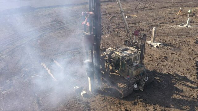 Excavation at a construction site, diesel pile driving machine with rumble and smoke drives piles deep into the ground to ensure the strength of the foundation of the future structure