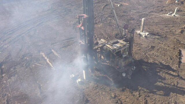 Excavation at a construction site, diesel pile driving machine with rumble and smoke drives piles deep into the ground to ensure the strength of the foundation of the future structure