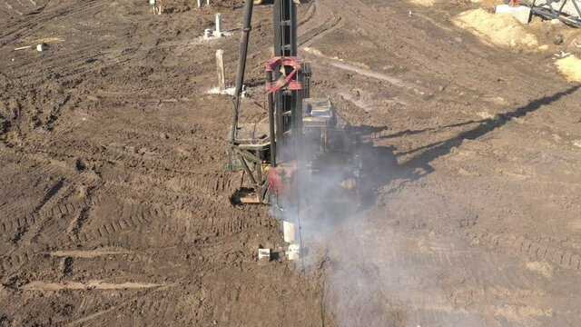Excavation at a construction site, diesel pile driving machine with rumble and smoke drives piles deep into the ground to ensure the strength of the foundation of the future structure
