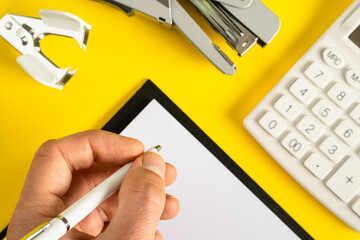 Mock up office accessories on yellow background flat lay of business gadgets and hand of unknown man holding pen writing