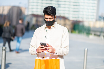 Man carrying shopping bags while using a smartphone, covid and coronavirus concept
