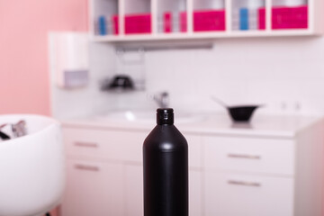 Fototapeta na wymiar Black bottle with hair care shampoo in hairdressing salon