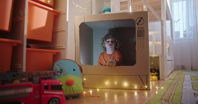 Adorable boy playing in carton TV. Cute boy playing and reading book while sitting inside handmade carton TV in playroom