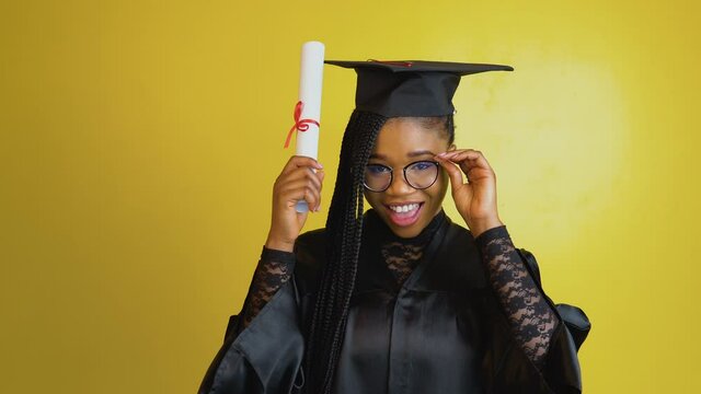 A joyful graduate student holds an international diploma and plays with her glasses and expresses happiness and positive emotions about her achievement. Doctor of Philosophy