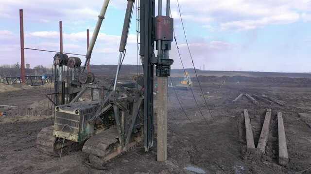 Excavation at a construction site, diesel pile driving machine with rumble and smoke drives piles deep into the ground to ensure the strength of the foundation of the future structure