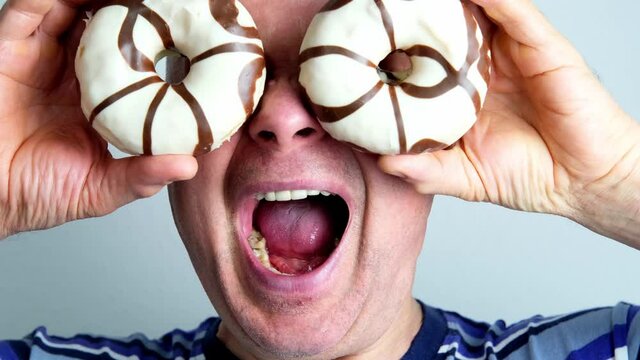 funny crazy middle-aged man put round donuts in glaze to his eyes, fooling around, showing grimaces, close-up head, concept of a good mood, a sense of humor, mental health