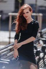 Beautiful redhead stylish girl in black dress outdoor