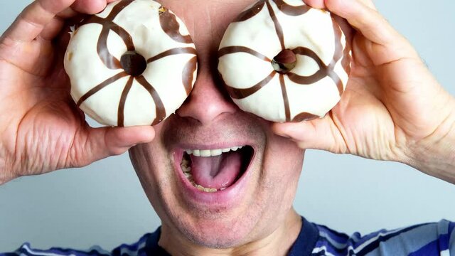 funny crazy middle-aged man put round donuts in glaze to his eyes, fooling around, showing grimaces, close-up head, concept of a good mood, a sense of humor, mental health