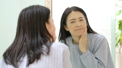 鏡を見ながら頬をさする女性