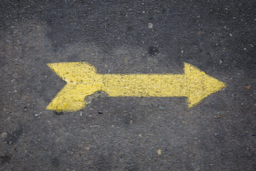 Yellow arrow painted on concrete sidewalk pointing right