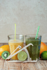 Tall glass with kiwi and spinach smoothie surrounded by fruits on a wooden table