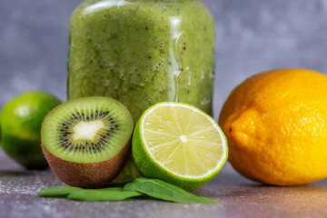 Fototapeta na wymiar Close-up of fresh kiwi and lime fruit halves against a smoothie mug on gray backdrop.