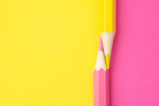 PINK AND YELLOW CRAYONS FACED AND ISOLATED ON THE SAME COLORS BACKGROUND. BACK TO SCHOOL. MINIMALIST CREATIVITY AND CRAFTS CONCEPT. TOP VIEW