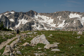 Fototapeta na wymiar Woman Hikes Alongside Alpine Meadow High in the Teton range