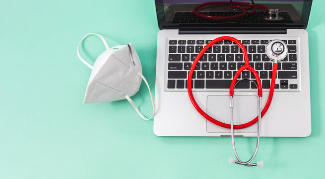Top view of a red stethoscope on a computer keyboard with a mask on a pastel green background. Concept of medicine, security and technology - Powered by Adobe