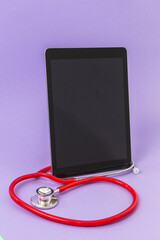 Tablet placed vertically wrapped by a red stethoscope on a purple background. Concept of medicine and technology