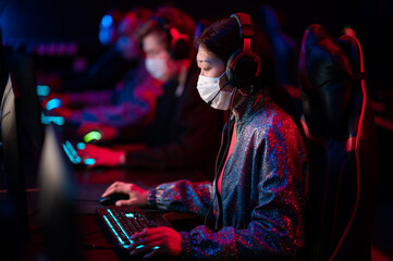 An online strategy tournament for esports players in the cyber games arena. A professional team of cyber-athletes competes with another crew, asian woman in a medical mask