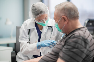 A young nurse in a mask gives a coronavirus vaccination to an elderly man in a clinic