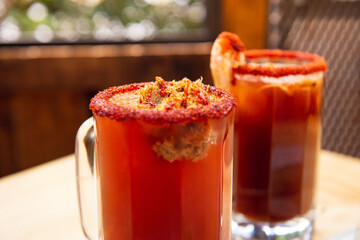 Michelada beer with tomato juice. Clamato with beer on wooden table. Mexican drink. Michelada beer with tomato juice, shrimps, clam and lemon, mexican drink cocktail in mexico. Concept of mexican beer