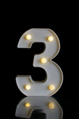 Number 3 (three), in a plastic part, with round flashing lights, with black background on a reflective surface