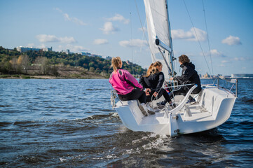 A fast, sporty, single-masted yacht with three athletes on board sails with a fair wind on a beautiful river.