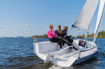 A fast, sporty, single-masted yacht with three athletes on board sails with a fair wind on a beautiful river.