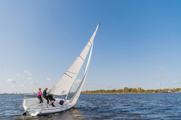 Naklejka premium A beautiful picture with a sports yacht on the background of an urban landscape floating under full sails on a wide river.