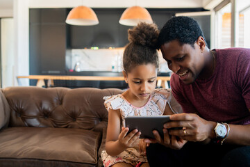 Father and daughter using digital tablet at home.