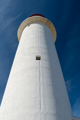 The watch room of a lighthouse.The lantern room has a large green bulb. The building is white with a red rail around the gallery deck.The background is cloudy and there's vignetting around the edges. 