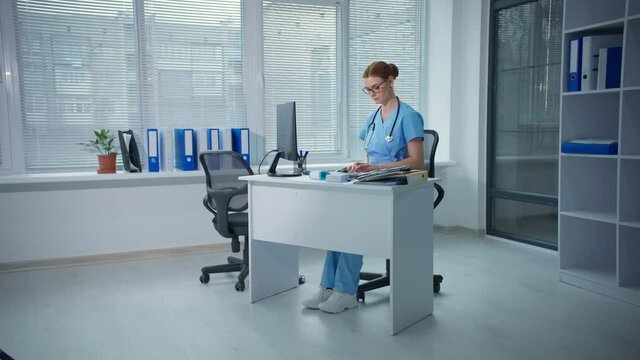 overworked family doctor works in a hospital office, female therapist types on computer keyboard then feels a headache while sitting at a table with documents
