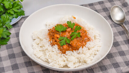 Rice with chicken meat cooked with paprika and sour cream, served with fresh parsley, close up on kitchen table