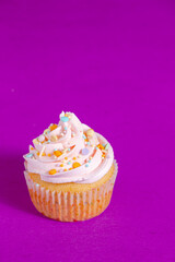 Pink frosted vanilla cupcakes with sprinkles on a bright purple background