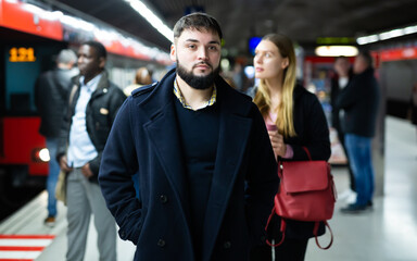 Portrait of young male passenger waiting for train on subway platform ..