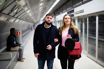 Young bearded man with his girlfriend wearing warm jackets walking on modern underground station