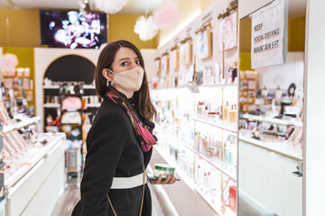 Young woman wearing face mask shopping sign Maintain Social Distance choosing beauty products in the store. New normal, protection, safety concept. Close up