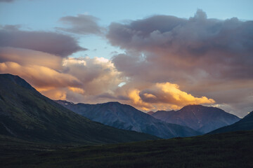 Beautiful mountain scenery with golden dawn light in cloudy sky. Scenic mountain landscape with illuminating color in sunset sky. Silhouettes of mountains on sunrise. Gold illuminating sunlight in sky