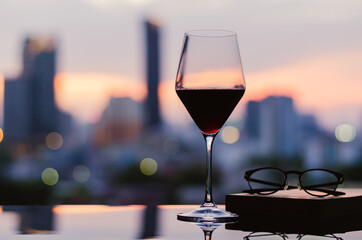 A glass of red wine with spectacles and book put on table with city background. Stay home concept.