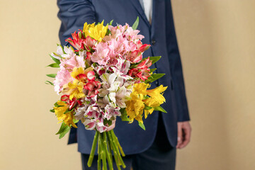 man in suit holds out a bouquet of multi-colored flowers. As a gift multi-colored alstroemerias, pink, yellow, purple, white and red alstroemerias.