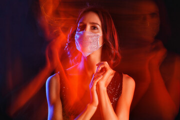 Beautiful young woman wearing a beaded mask on a black background. Mixed neon light.