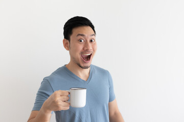 Funny wow face of Asian man in blue t-shirt drinks coffee from white mug.