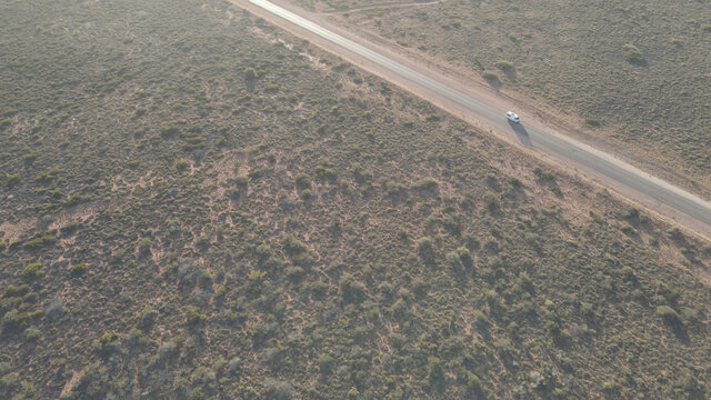 Car Driving Over Rural Road In The Australian Desert With A Long Shadow During Golden Hour In Exmouth, Western Australia. Angle Aerial Drone Shot