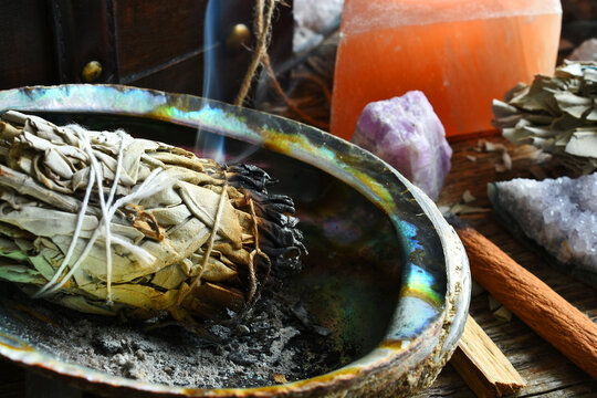 A close up image of a burning white sage smudge stick with selenite candle.