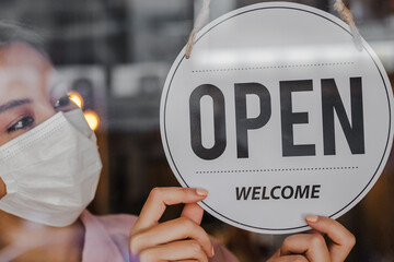 Smiling young asian owner retail,coffee shop woman turning sign board to open wearing face...