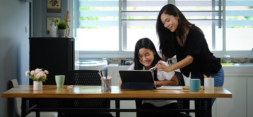 Asian mother helping her daughter doing homework with digital tablet at home.
