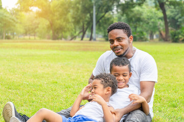 Naklejka na ściany i meble Cheerful african american father and two sons playing in park, Happiness family concepts, parent and childs play in park