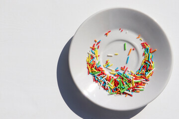 Rainbow sugar sprinkle dots, decoration for cake and bakery in plate on white table. Colorful...